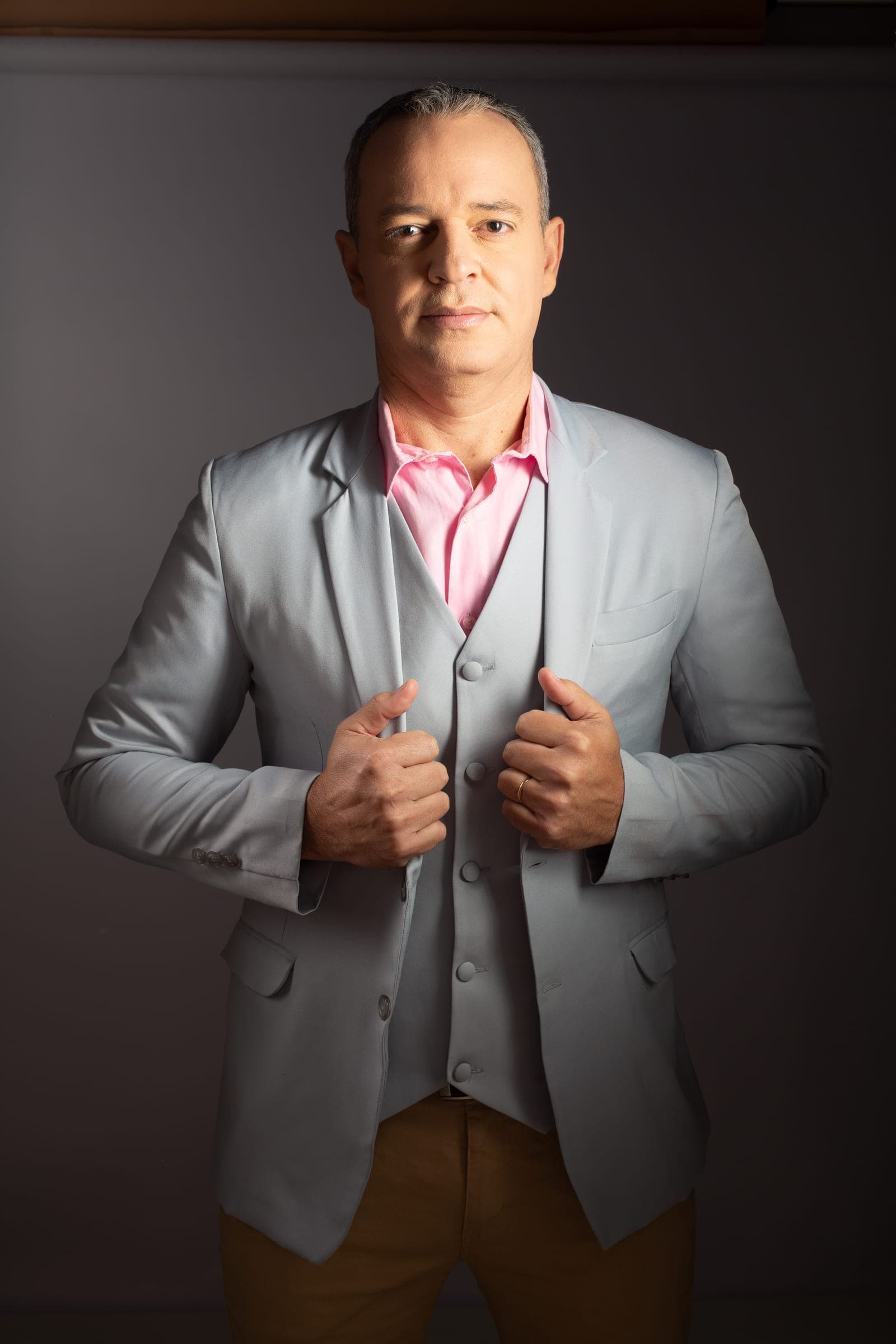 Paulo Crispim em retrato de estúdio, vestindo camisa rosa e terno cinza
